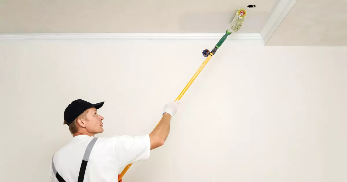 A man painting a ceiling using a long roller brush